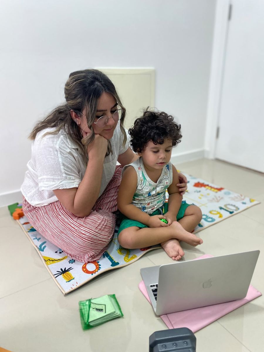 Fonoaudióloga e criança sentadas no tapete durante atividade